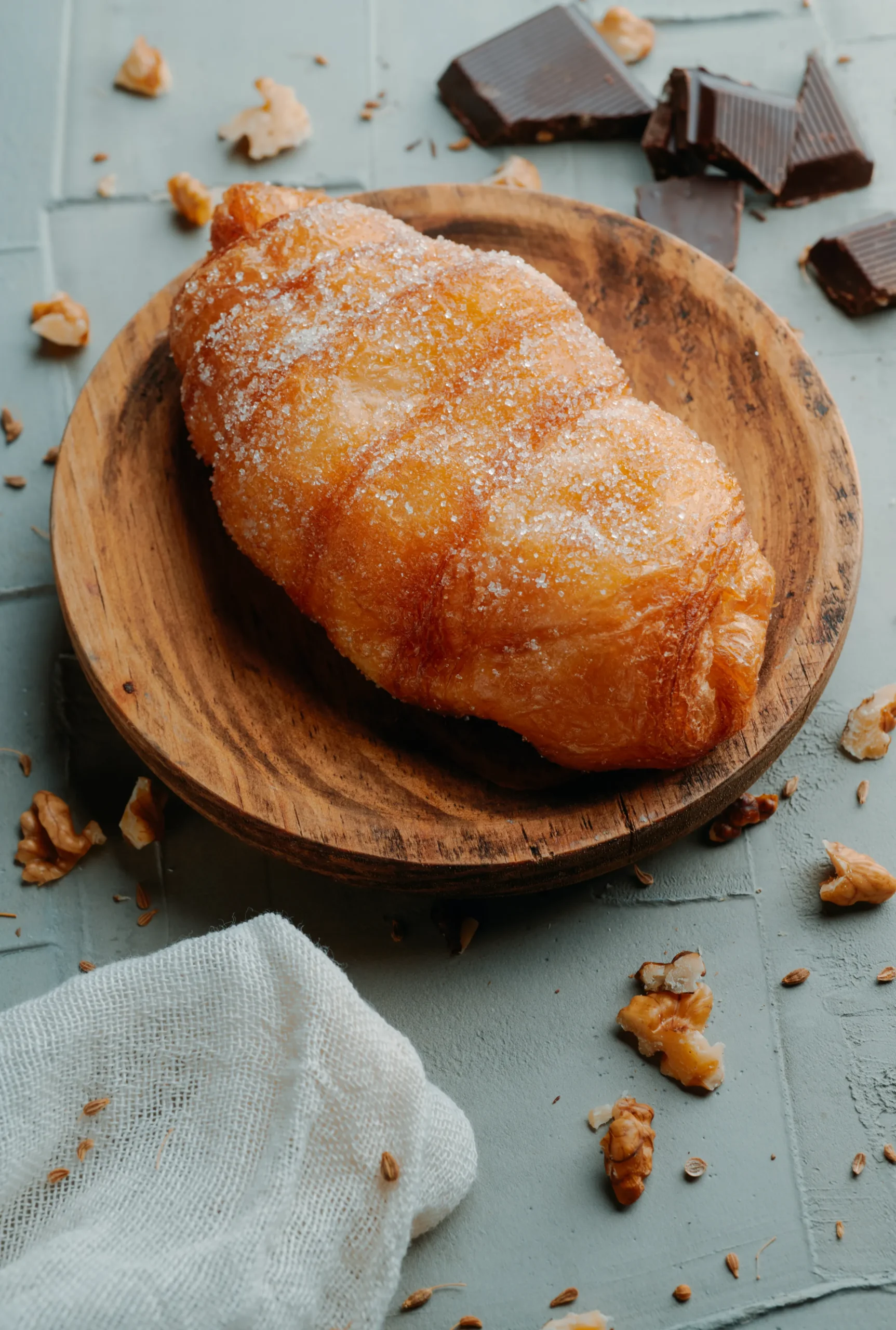 Grand Tour of Catalonia | A xuixo de crema, a pastry filled with custard typical of catalonia, spain, on a wooden plate, placed on a textured gray surface with some bits of chocolate