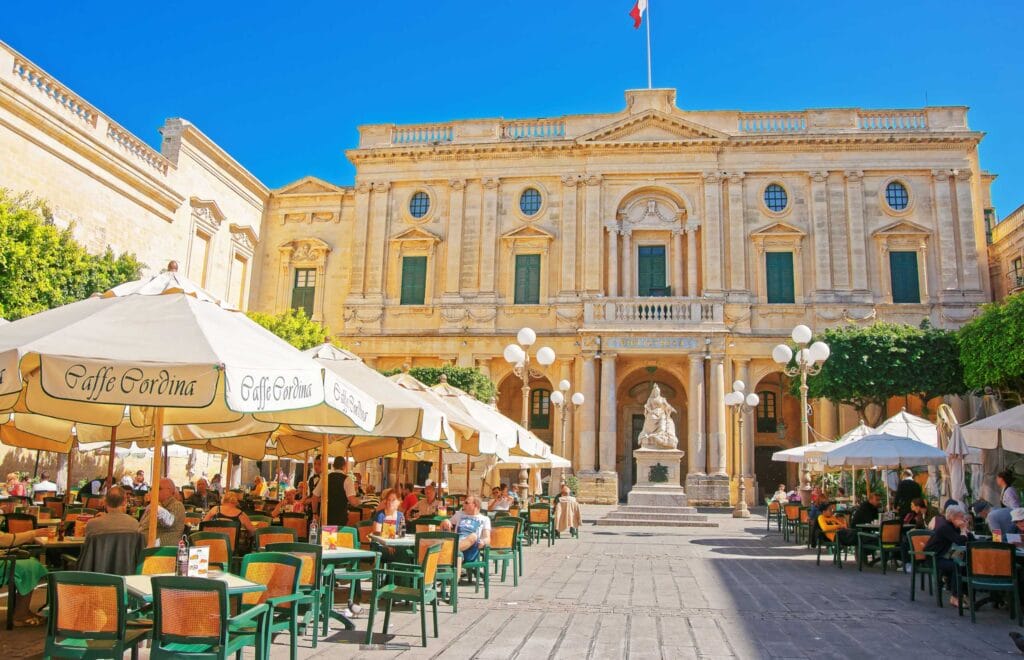People resting in open air cafes at Republic Square with National Library in Valletta old town, Malta