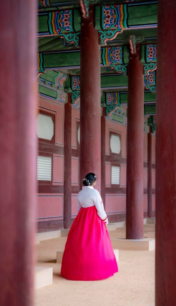 Unrecognizable young Latina dressed in a traditional pink and white hanbok, at Gyeongbokgung Palace corridor and ornate columns, Seoul, South Korea | Seoul city guide