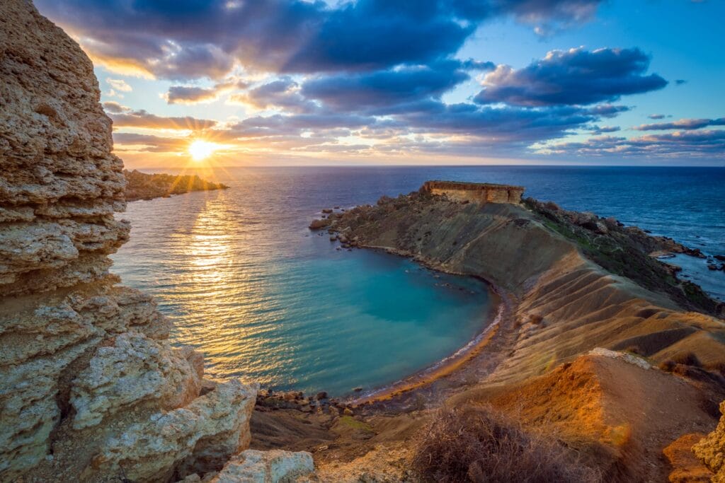 Coastal landscape shows a striking sunset over Ġnejna Bay