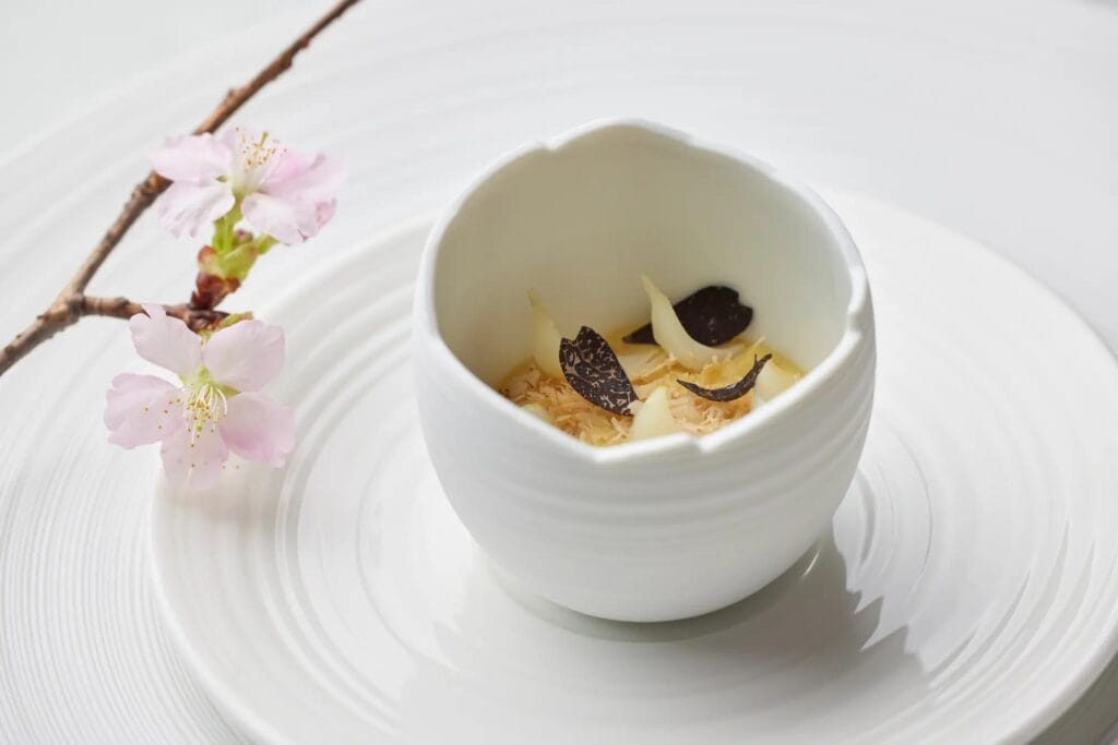 Black truffle slices and white petals, served in a ribbed white ceramic bowl