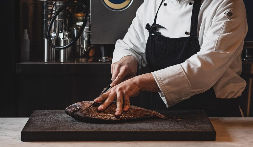 A private chef preparing and scoring a whole fish