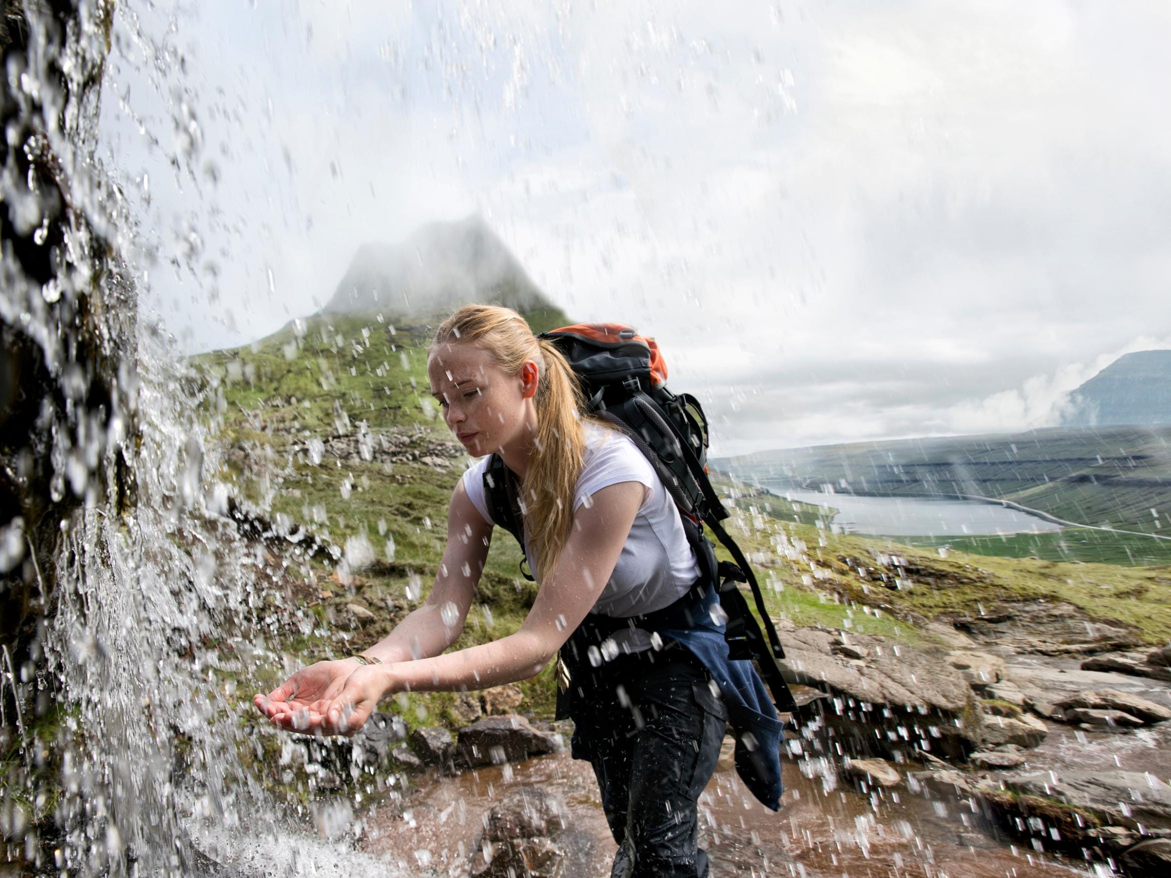 A hiker catching fresh water from a mountain spring in the Faroe Islands