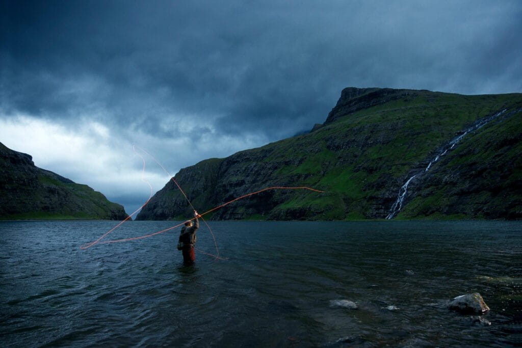 Fly fishing in a scenic lake surrounded by green mountains and a waterfall in the Faroe Islands